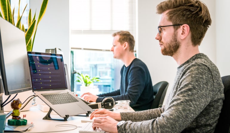  Two men working on computers at neighboring desks.